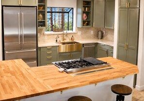 Cocina moderna con una isla central, electrodomésticos de acero inoxidable y vistas a árboles a través de una ventana.