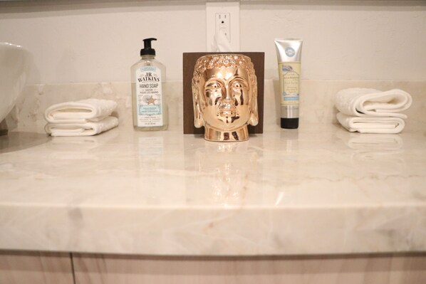 A bathroom counter with neatly folded towels, a gold Buddha statue, and toiletries including hand soap and lotion.