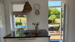 Een moderne keuken met witte kasten, een zwart aanrecht en een hanglamp. Er is een raam met uitzicht op de omgeving, en een deur die leidt naar een terras.