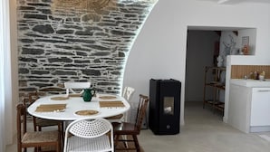 Een eethoek met een stenen muur, een ronde tafel met stoelen, en een keuken op de achtergrond.