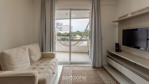 A living room with a sofa, a flat-screen TV, a balcony with a hammock, and a patterned rug. - Apt W/bbq, 850m From Ingleses Beach Vde101 (Florianópolis)