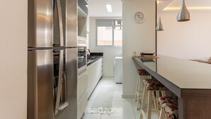 A modern kitchen with stainless steel appliances, a large window, and a bar area with stools. - Apt W/bbq, 850m From Ingleses Beach Vde101 (Florianópolis)