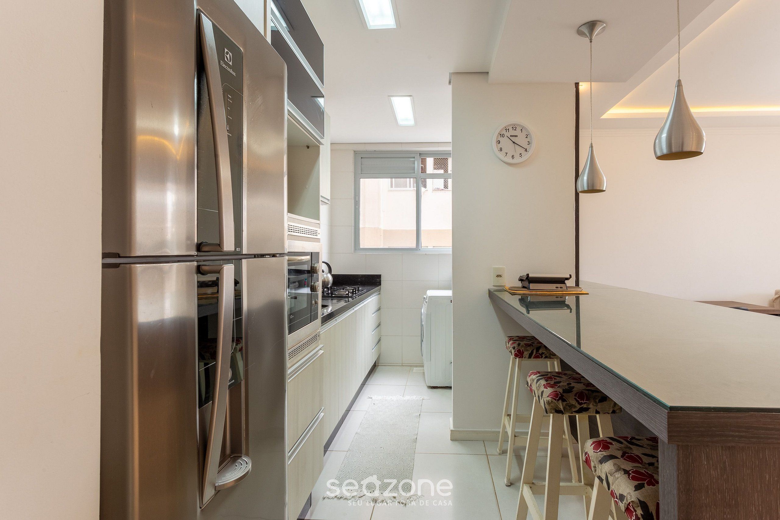 A modern kitchen with stainless steel appliances, a large window, and a bar area with stools.