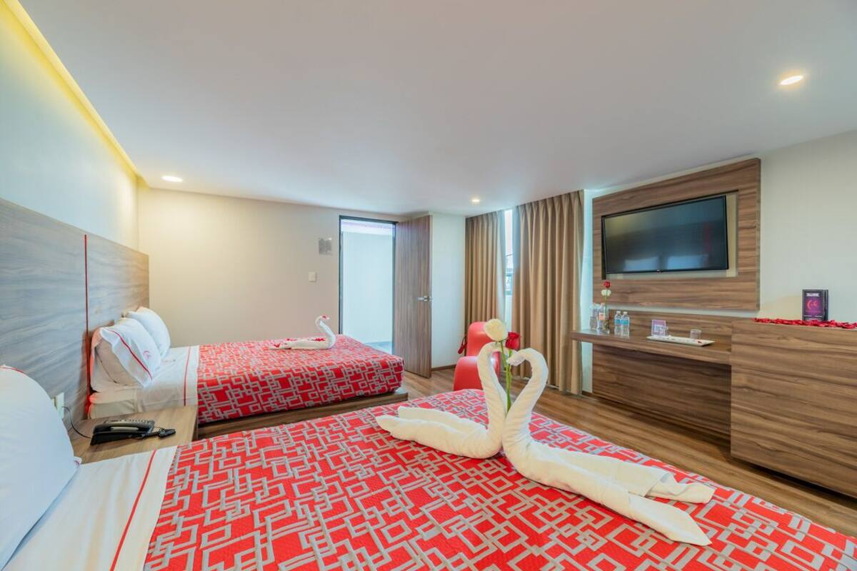 A hotel room with two beds, a TV, a desk, and a red and white patterned carpet.