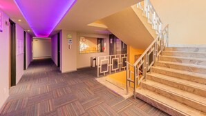 A hotel hallway with a herringbone-patterned floor, a staircase with a wooden railing, and purple ambient lighting. - Hotel Ecatepec (Ecatepec de Morelos)