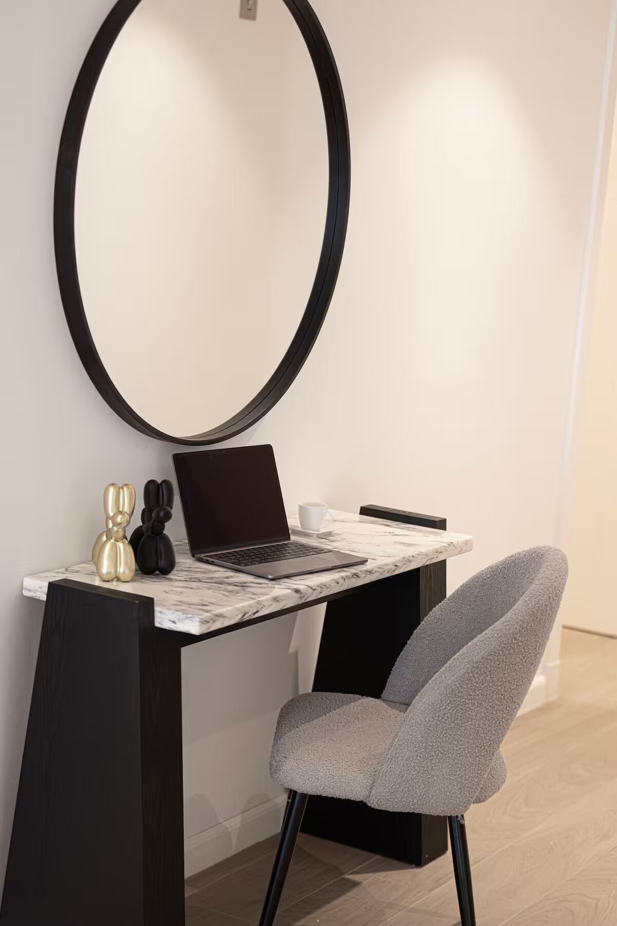 A modern desk with a laptop, a cup, and two decorative items on a marble surface.