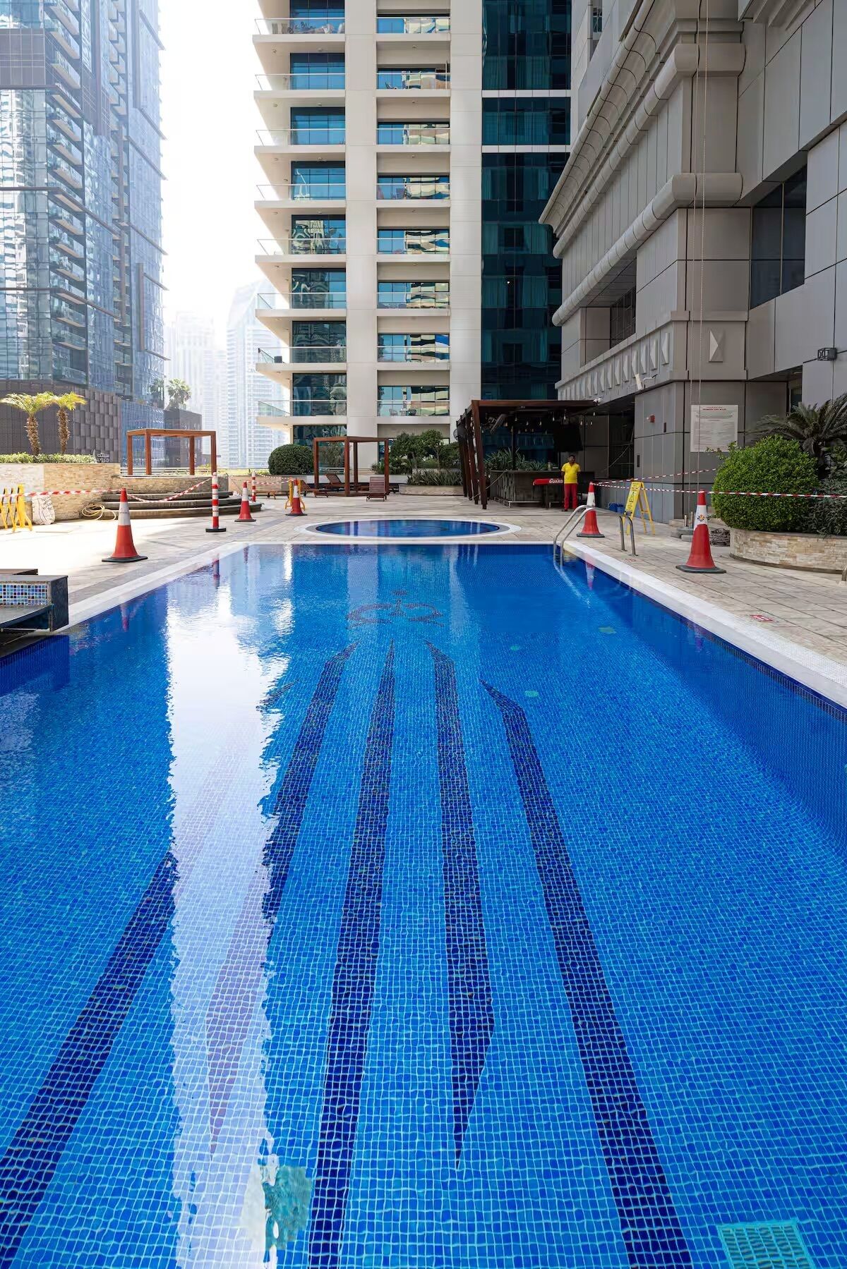 Ein Swimmingpool mit blau-gefliesten Mosaikmustern, umgeben von einem modernen Gebäude mit Balkonen und einer überdachten Sitzgelegenheit.