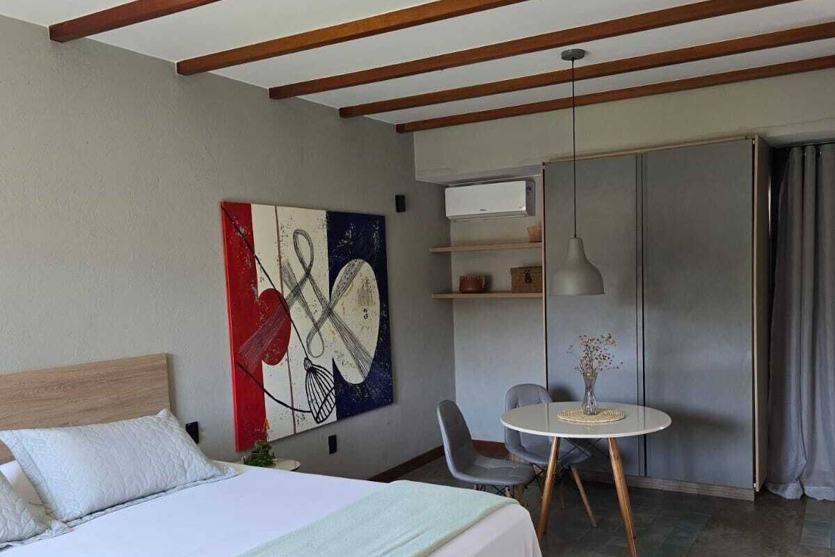 A hotel room with a bed, a dining table, a chair, a painting on the wall, and a wardrobe.