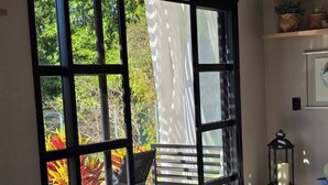 A room with a large sliding glass door leading to a balcony with a chair and potted plants. - Confraria Da Prata Flats (Pirenópolis)