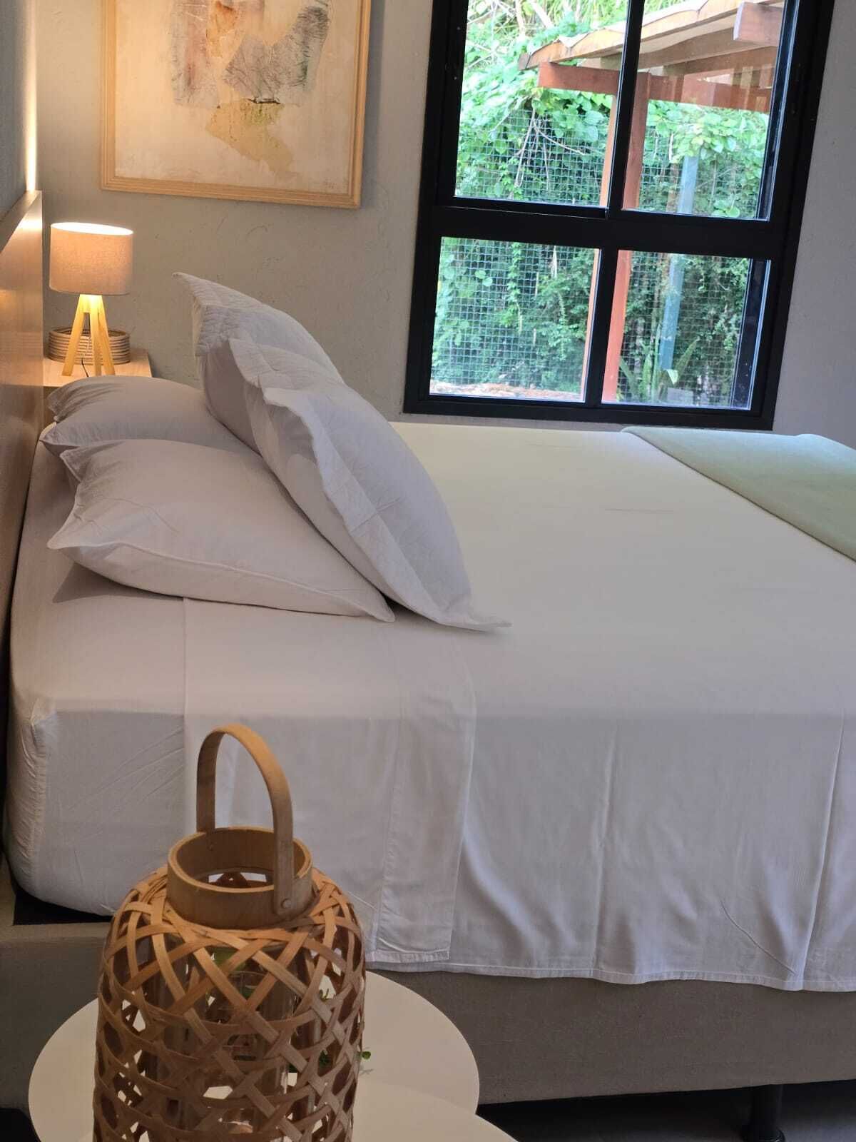 Een net opgemaakt bed met witte lakens, een houten nachtkastje met een lamp en een rieten lantaarn.