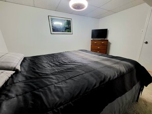 A bedroom with a bed, a dresser, a television, and a framed picture on the wall. - Stylish, Modern & Cozy Garden Apartment near Chicago (Beecher)