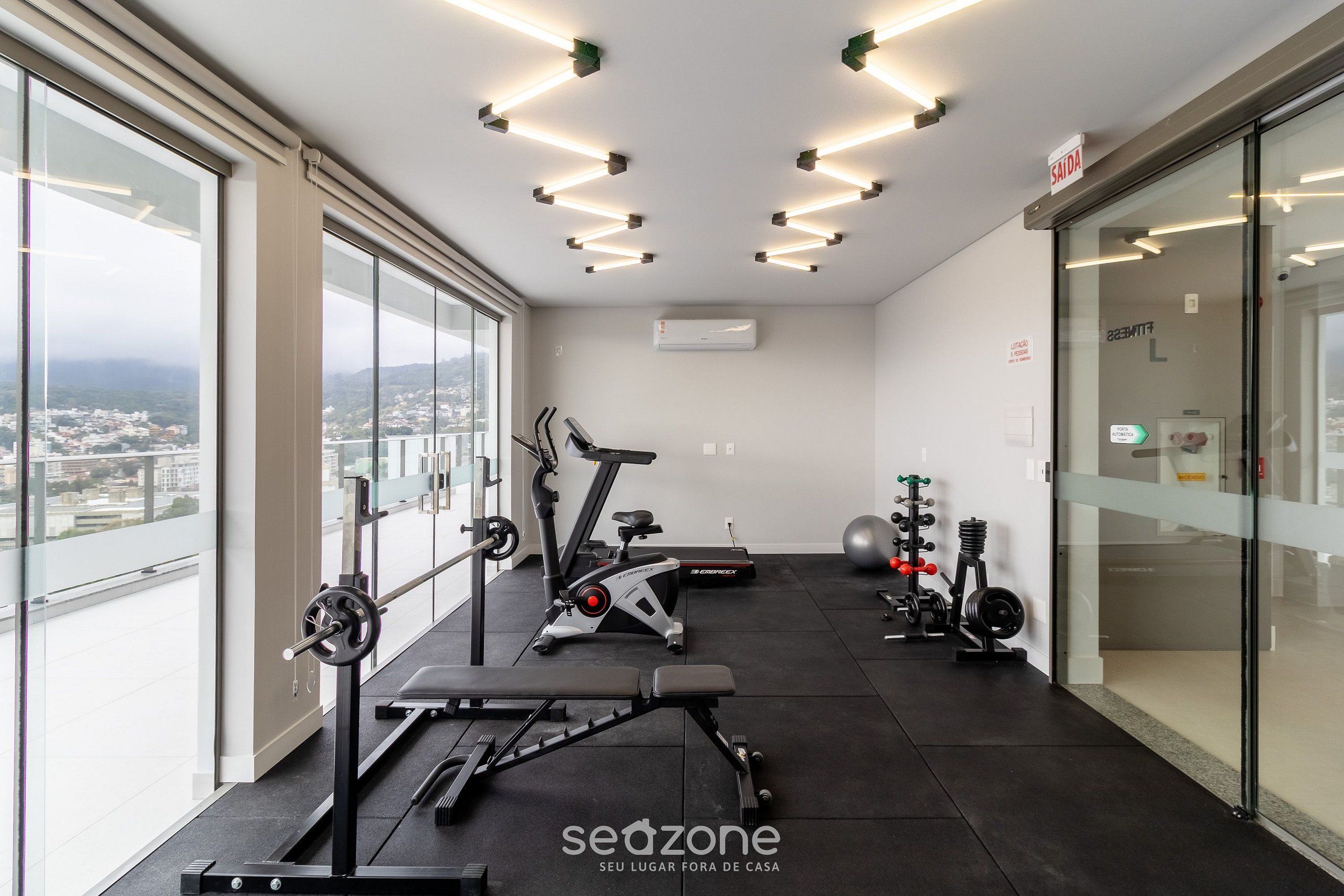 A modern gym with exercise equipment, large windows, and a city view.
