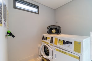 A laundry area with a washing machine and dryer, a small window, and a wall-mounted security camera. - Apartments Just a few Minutes From Ufsc, Condo With Laundry Facilities (Florianópolis)