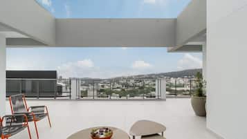 A modern balcony with a clear view of a cityscape, two chairs, a table, and a potted plant.