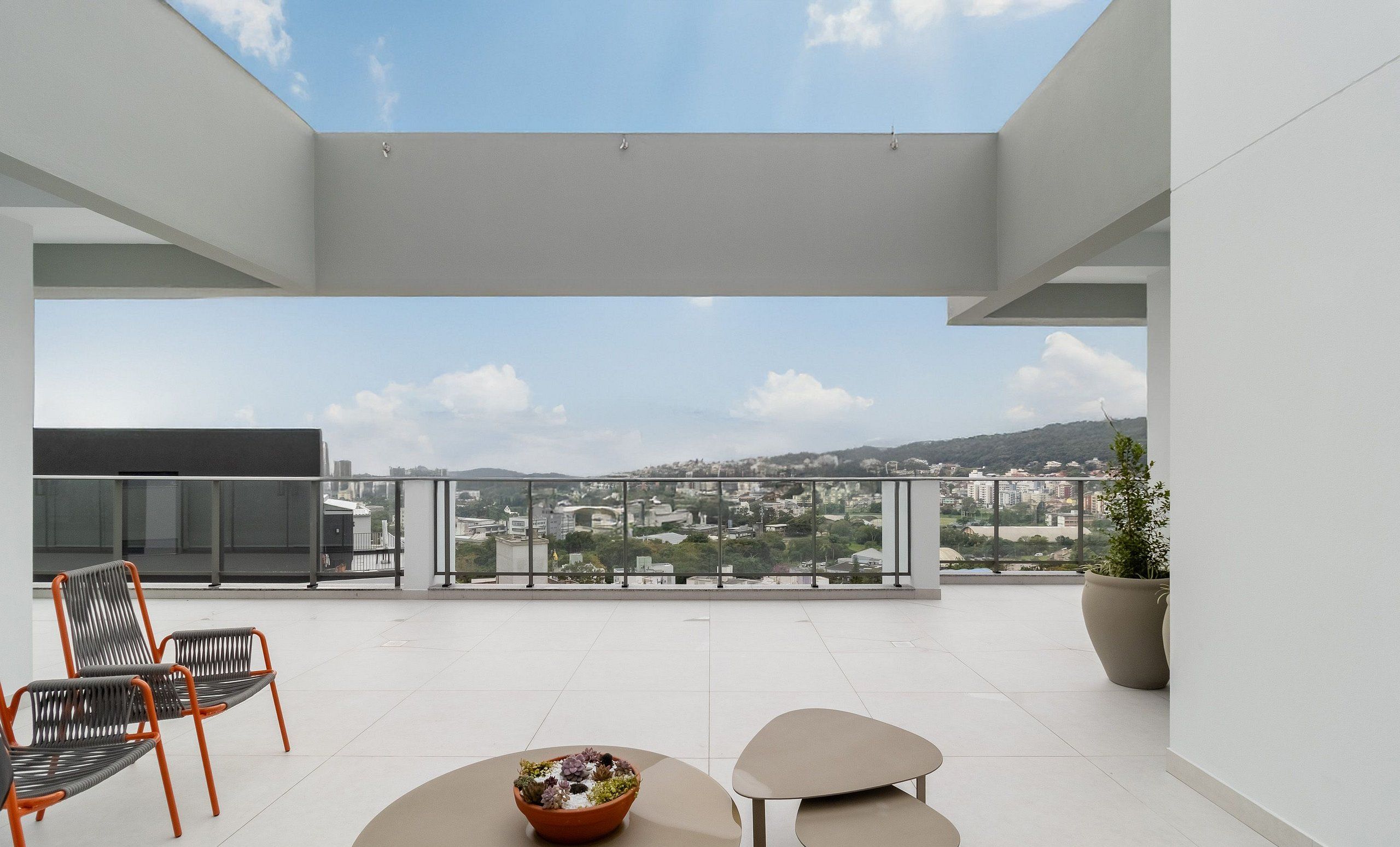 A modern balcony with a clear view of a cityscape, two chairs, a table, and a potted plant.