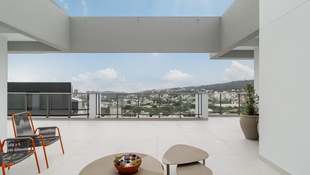 Ein moderner Balkon mit freiem Blick auf eine Stadtlandschaft, zwei Stühle, ein Tisch und ein Blumentopf.