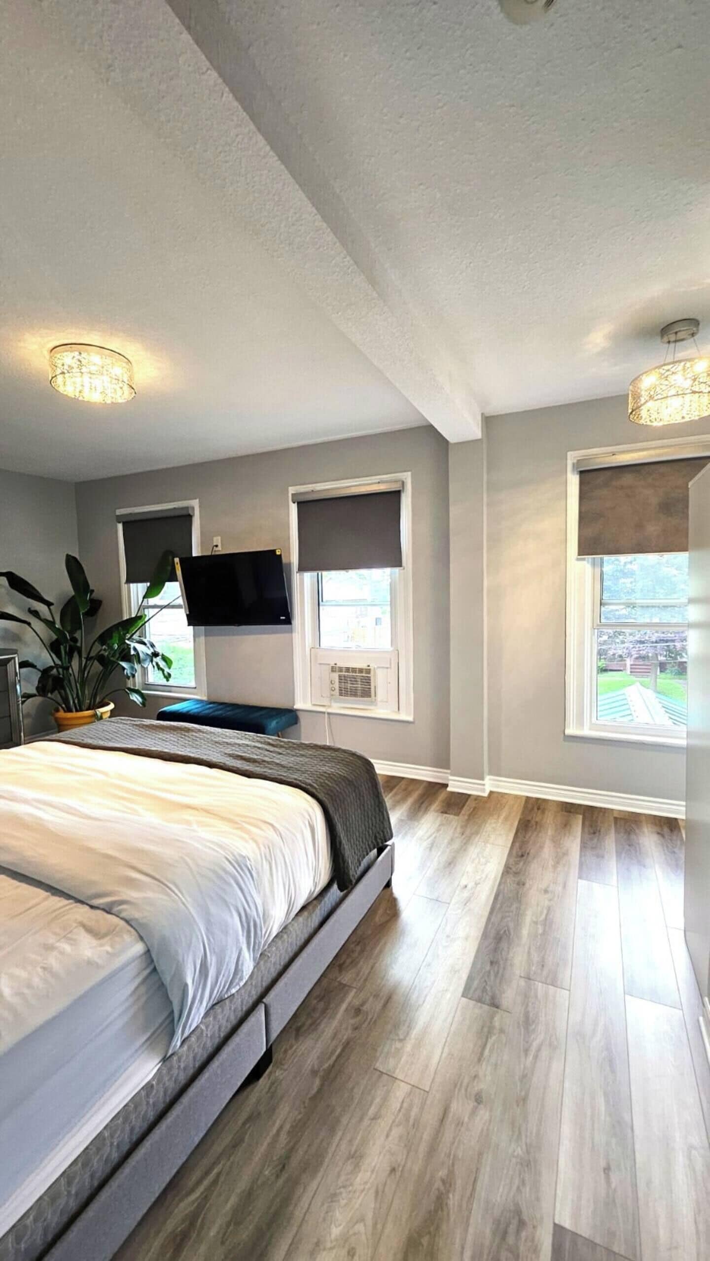Une chambre à coucher avec un lit, un téléviseur fixé au mur et deux fenêtres équipées de stores.