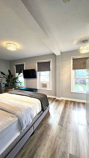 Un dormitorio con una cama, un televisor montado en la pared y dos ventanas con persianas.