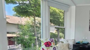 Una habitación con un asiento junto a la ventana, una cesta de frutas y una pequeña mesa con botellas y un cuaderno.