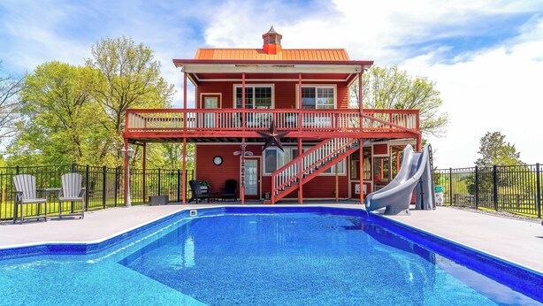 Un edificio de dos pisos con fachada roja, un balcón y un tobogán que desemboca en una piscina.