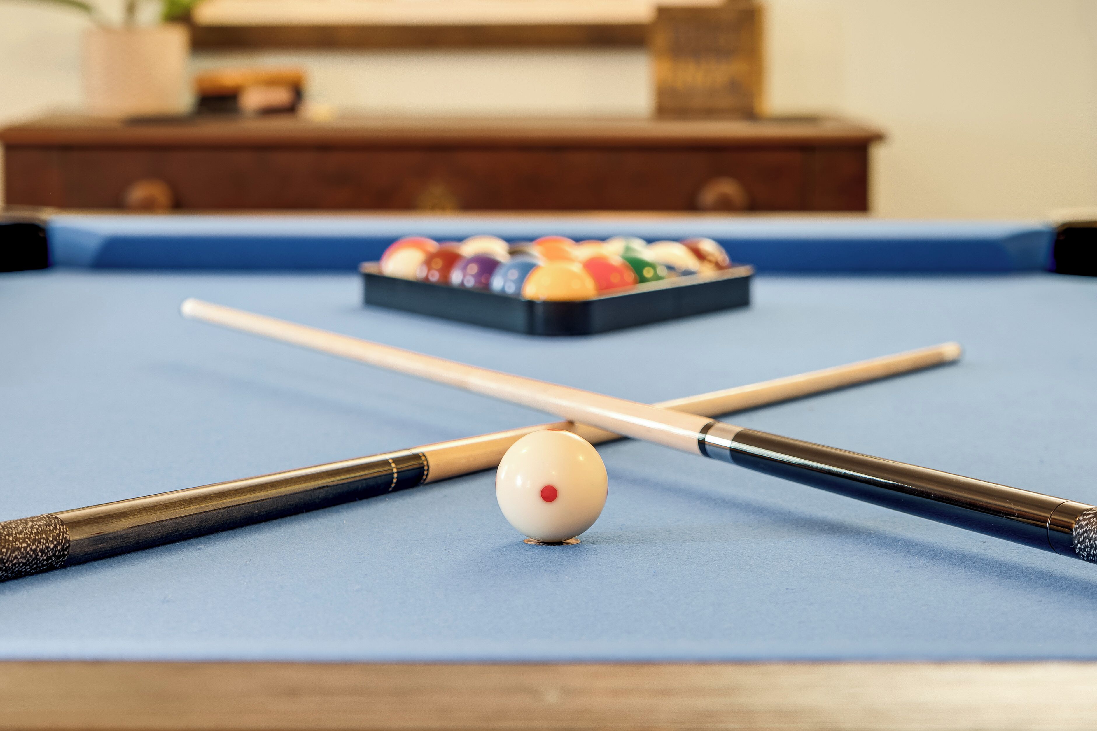 A pool table with a white cue ball, two pool cues, and a set of colorful balls in the background.