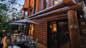 Eine Blockhütte mit einer Terrassenfläche, die Sitzgelegenheiten und einen großen Sonnenschirm bietet.