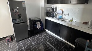 A modern kitchen with black cabinets, a refrigerator, a coffee machine, and a sink.
