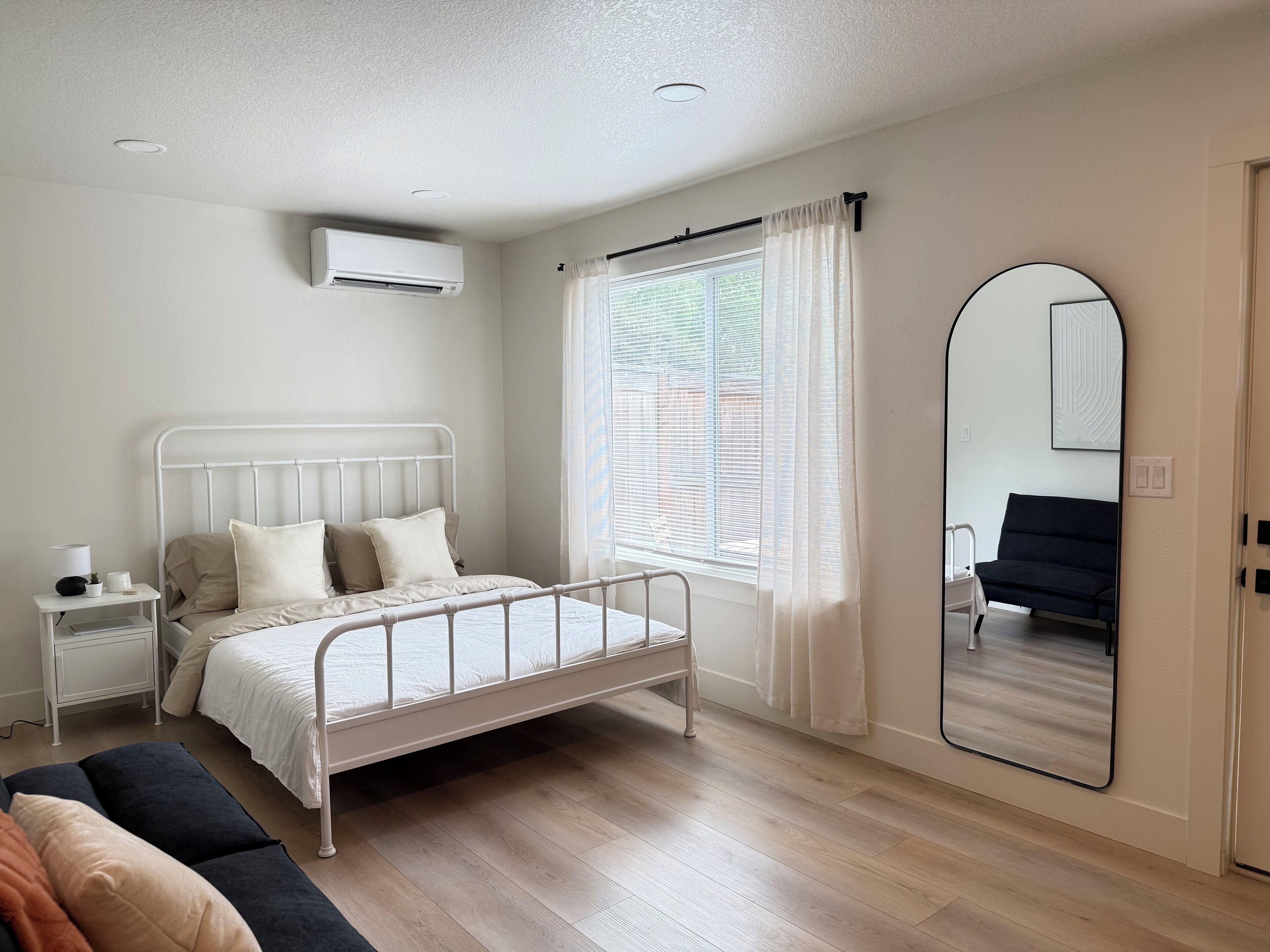 A bedroom with a bed, bedside table, and a large mirror.