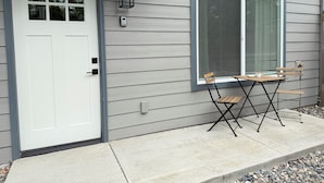 Una casa con puerta blanca, ventana con persianas y un pequeño patio con mesa y sillas.