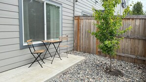 Un patio con una mesa y sillas de madera, un árbol pequeño y una valla de madera.