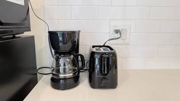 A coffee maker and toaster on a kitchen counter with white tiled backsplash and a power outlet.