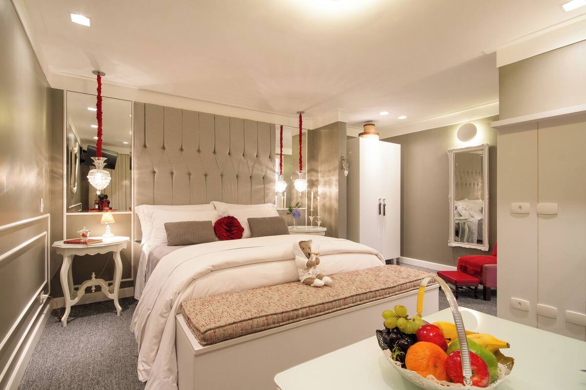 A modern bedroom with a large bed, bedside tables, a mirror, and a fruit basket.