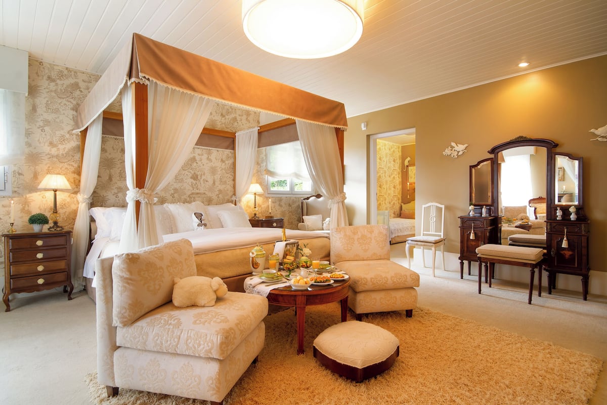 A bedroom with a canopy bed, a sitting area with a coffee table, and a dresser with a mirror.
