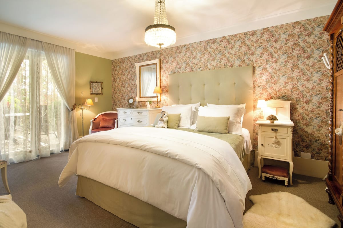 A bedroom with a large bed, a nightstand, a dresser, a mirror, and a chandelier.