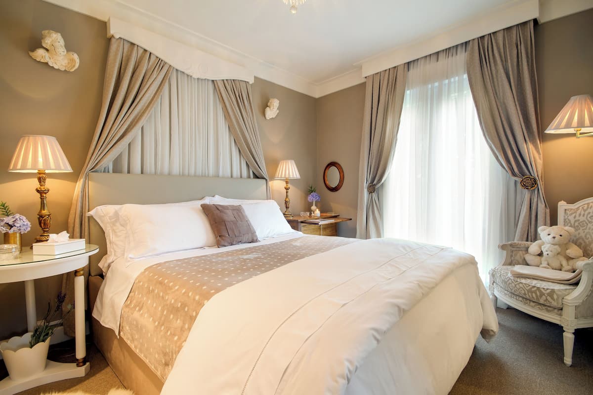 A neatly arranged hotel room with a large bed, two bedside tables with lamps, a chair, and a decorative mirror.