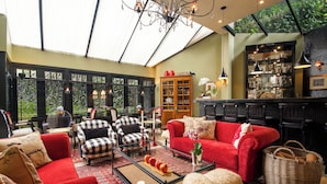 A spacious living area with a red sofa, black and white checkered chairs, a glass coffee table, and a large window with blinds. - Hotel Boutique Casa Regaleira (Campos do Jordão)