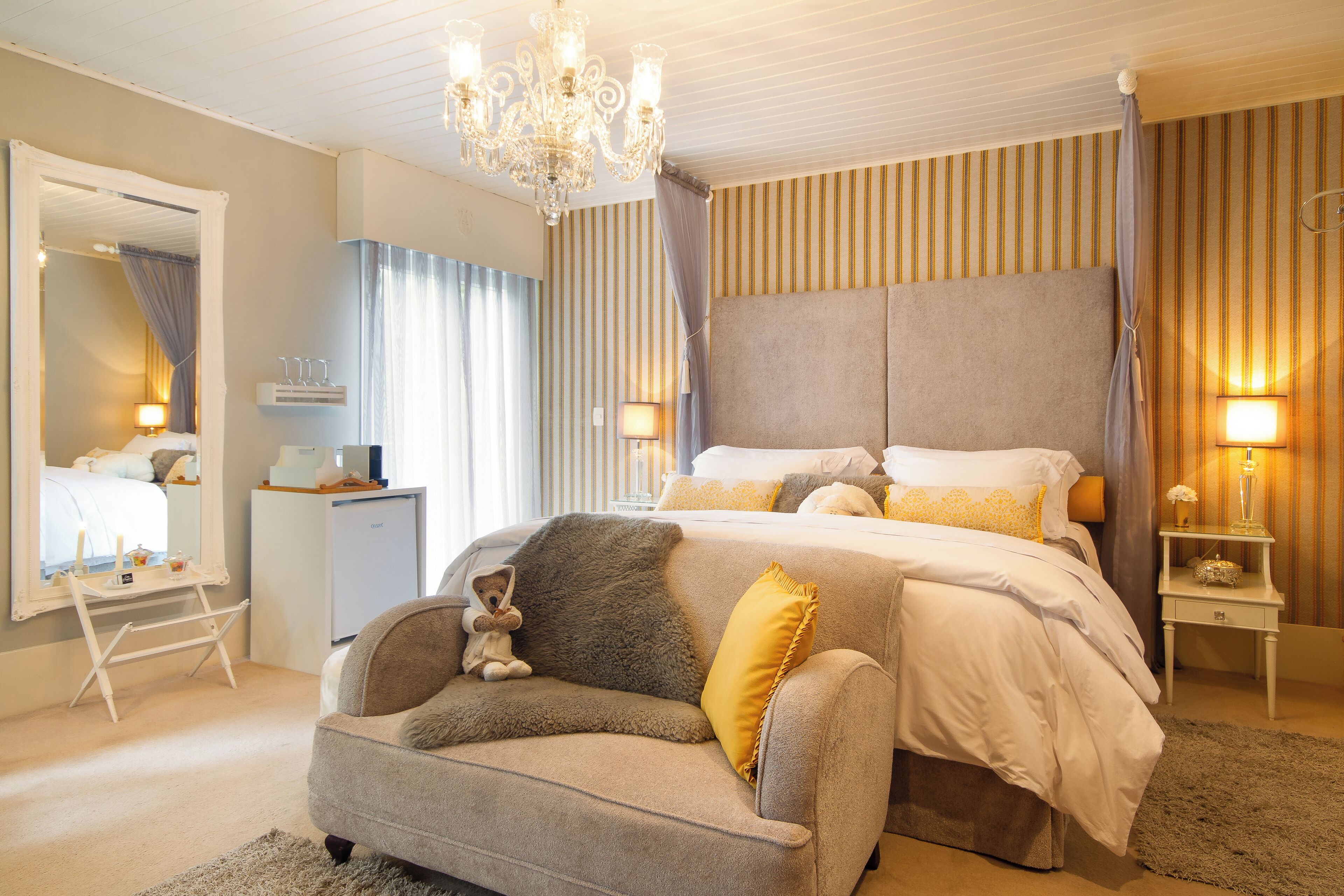 A bedroom with a large bed, a bedside table, a nightstand, a chair, a mirror, and a chandelier.