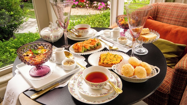 A table set with tea, sandwiches, and fruit, with a garden view. - Hotel Boutique Casa Regaleira (Campos do Jordão)
