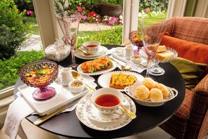 Una mesa servida con té, sándwiches y fruta, con vistas a un jardín.