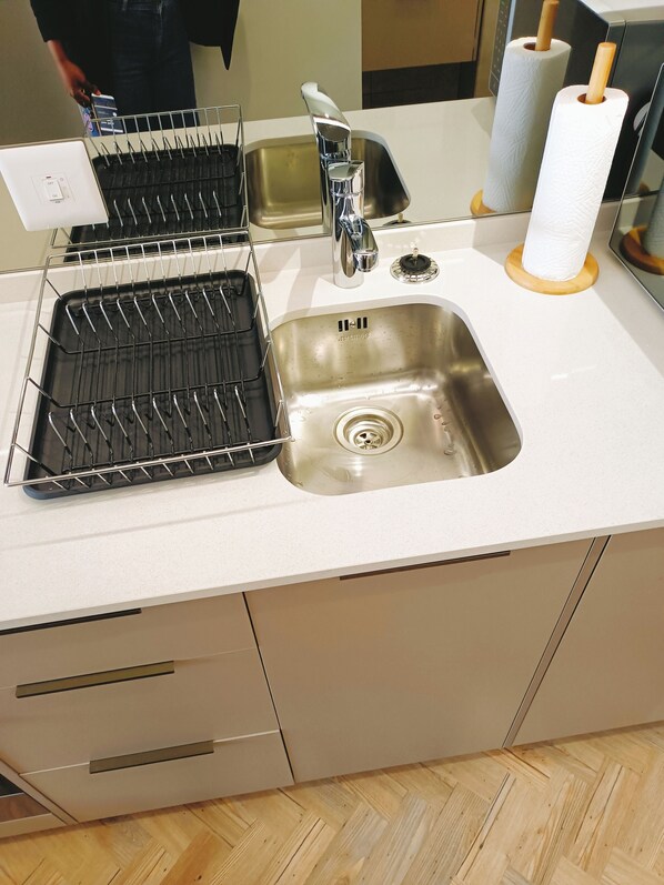 A kitchen with a stainless steel sink, a dish rack, and a wooden cutting board.