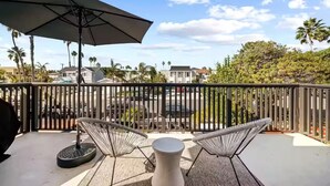 A balcony with a view of a parking area and houses, featuring two chairs and a table. - Pacific Beach Bayside Studio (San Diego)