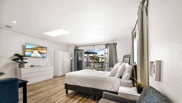 A modern bedroom with a bed, a desk, a chair, and a balcony with a view. - Pacific Beach Bayside Studio (San Diego)