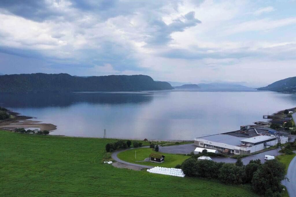 A large building with a flat roof, surrounded by a green field and a body of water.