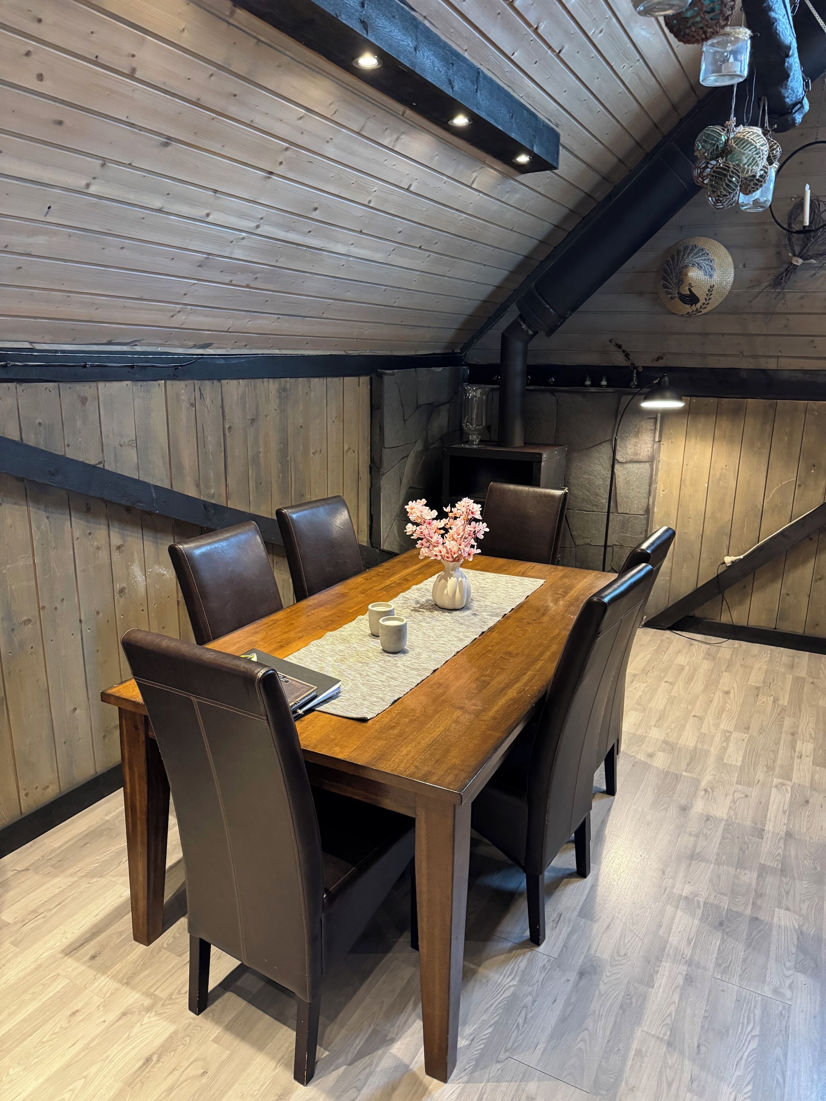 Un comedor con una mesa de madera, seis sillas, un florero con flores y una chimenea.