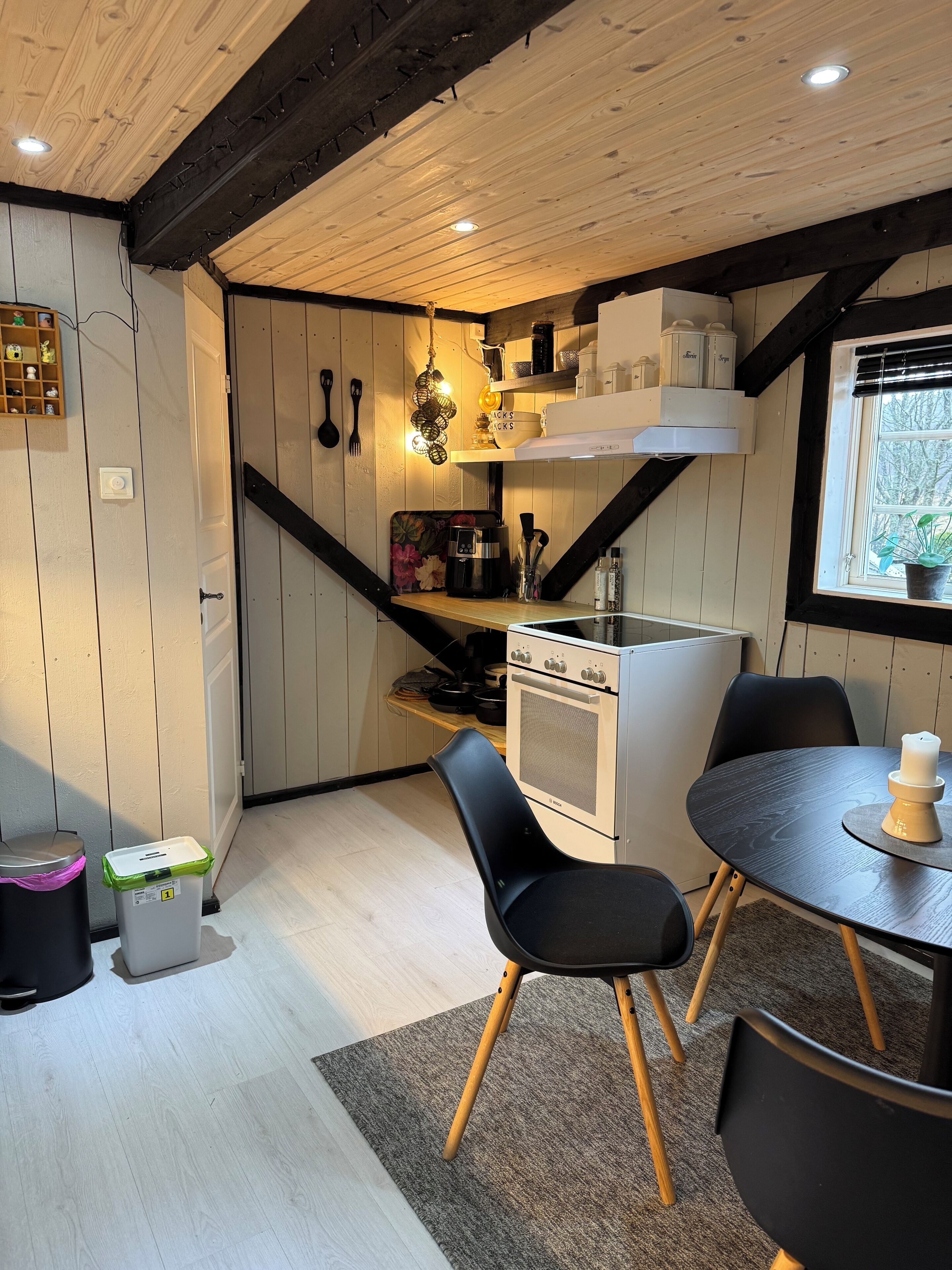 A compact kitchen with a stove, dining table, chairs, and a window with a view.