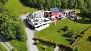 Un vaste domaine comprenant plusieurs bâtiments, dont une maison principale et plusieurs dépendances, le tout entouré de pelouses et d’arbres bien entretenus.