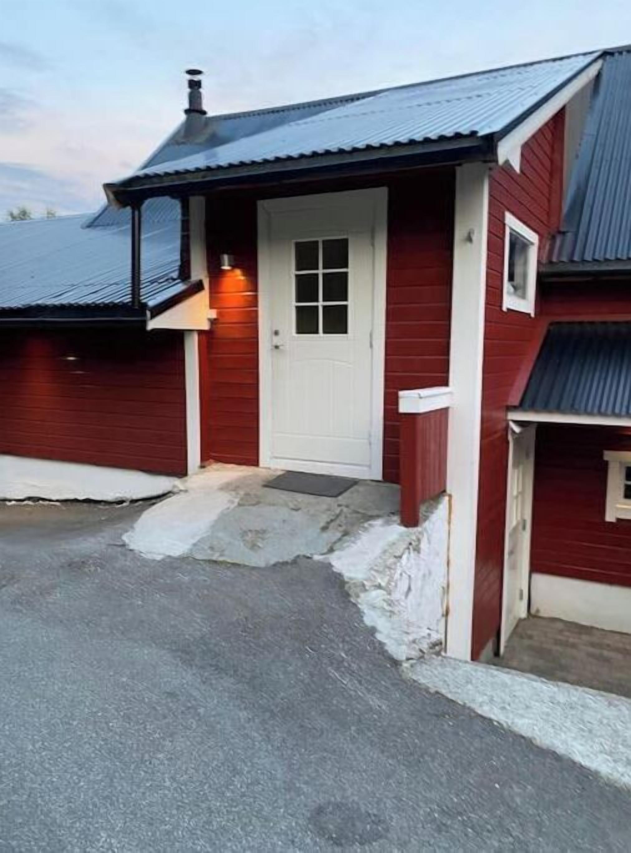 Un bâtiment rouge avec une porte blanche, un petit porche et un garage.
