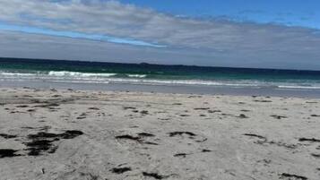 A sandy beach with footprints and a clear view of the ocean under a blue sky.