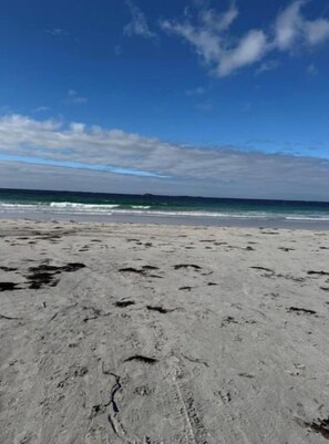 A sandy beach with footprints and a clear view of the ocean under a blue sky. - Eidsviklaaven (Møre og Romsdal)