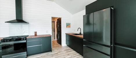 A modern kitchen with a large black refrigerator, dark cabinetry, and a wooden countertop.